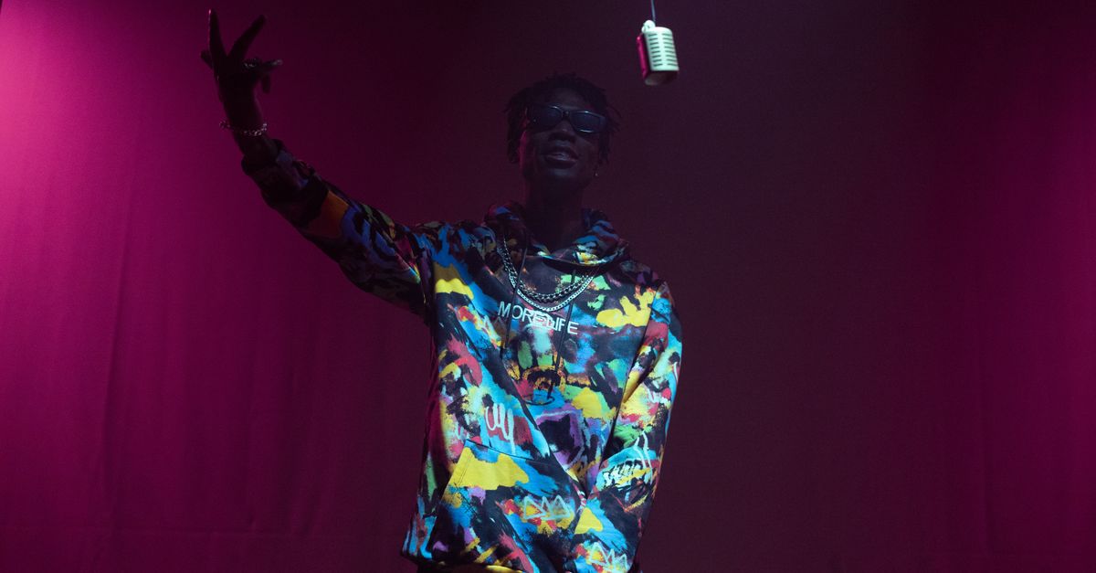 Engaging hip hop artist performing on stage with vintage microphone and vibrant fashion.